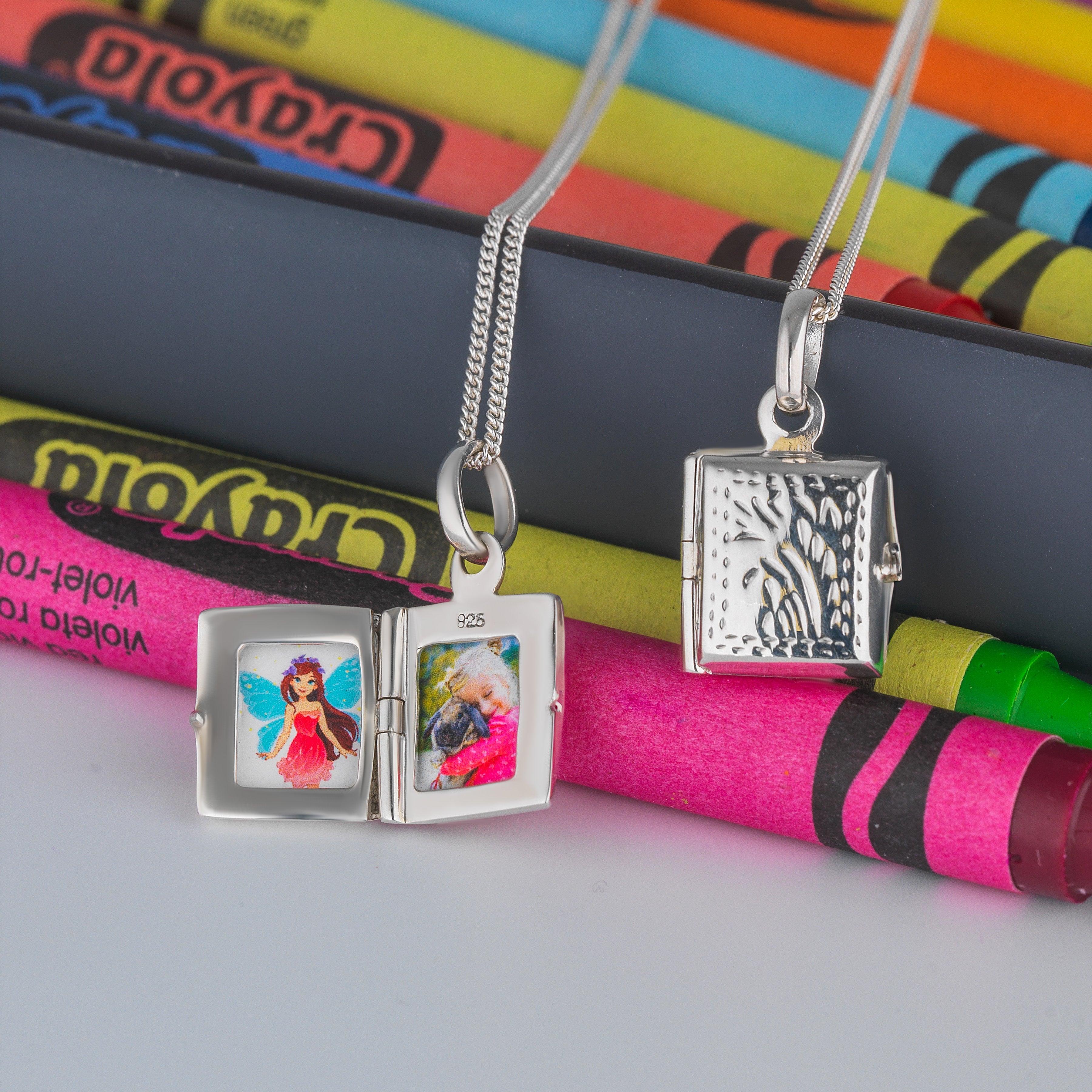 a 925 sterling silver book locket for children with a traditional foliate design on the front of the locket placed on a curb chain.