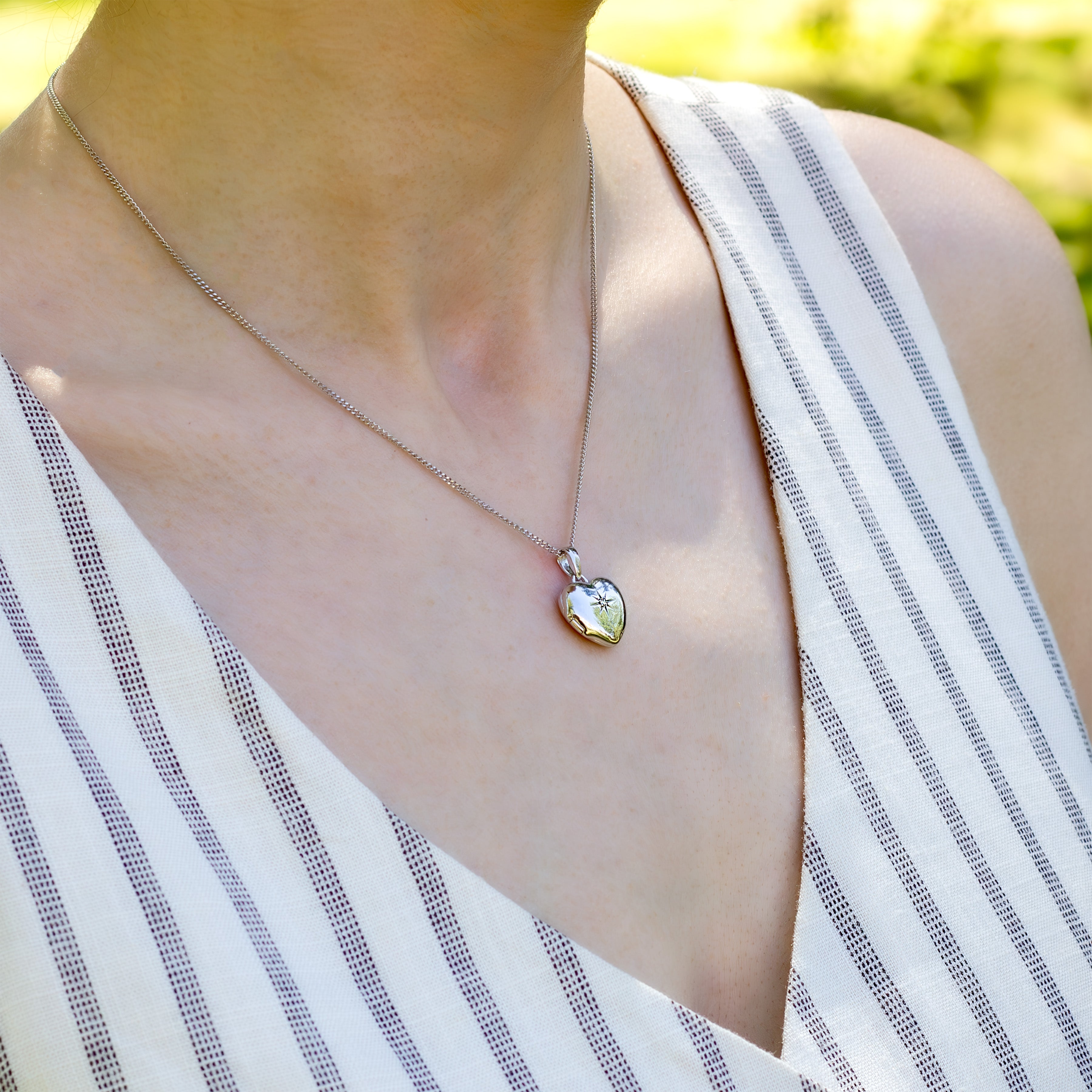 Model wearing a premium petite white gold heart locket with a star set diamond in the middle and placed on a curb chain.