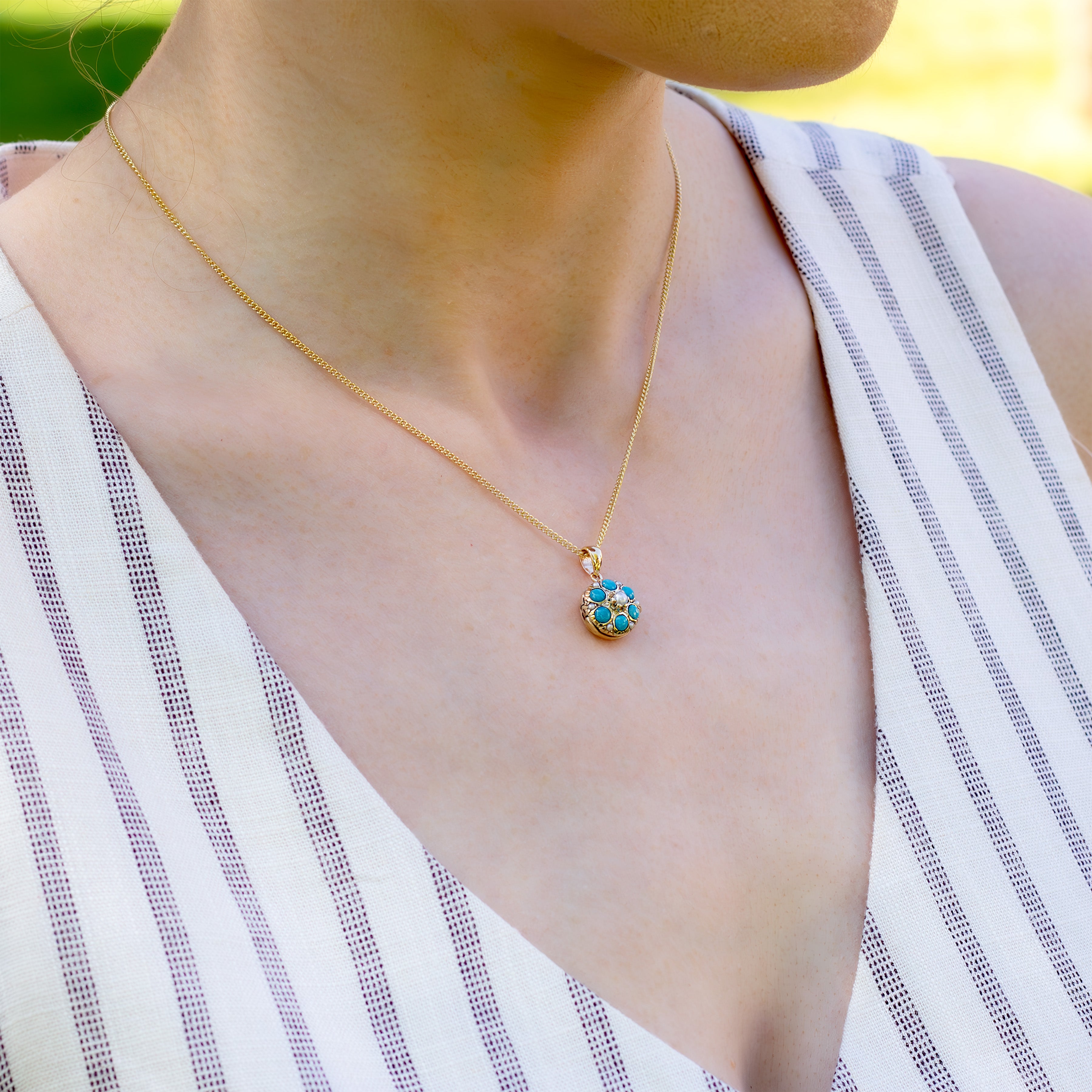 Model wearing a round 9 ct gold locket with real round turquoise and matching pearls spread throughout and placed on a modern 9ct gold base. Matched with a 9ct gold curb chain.