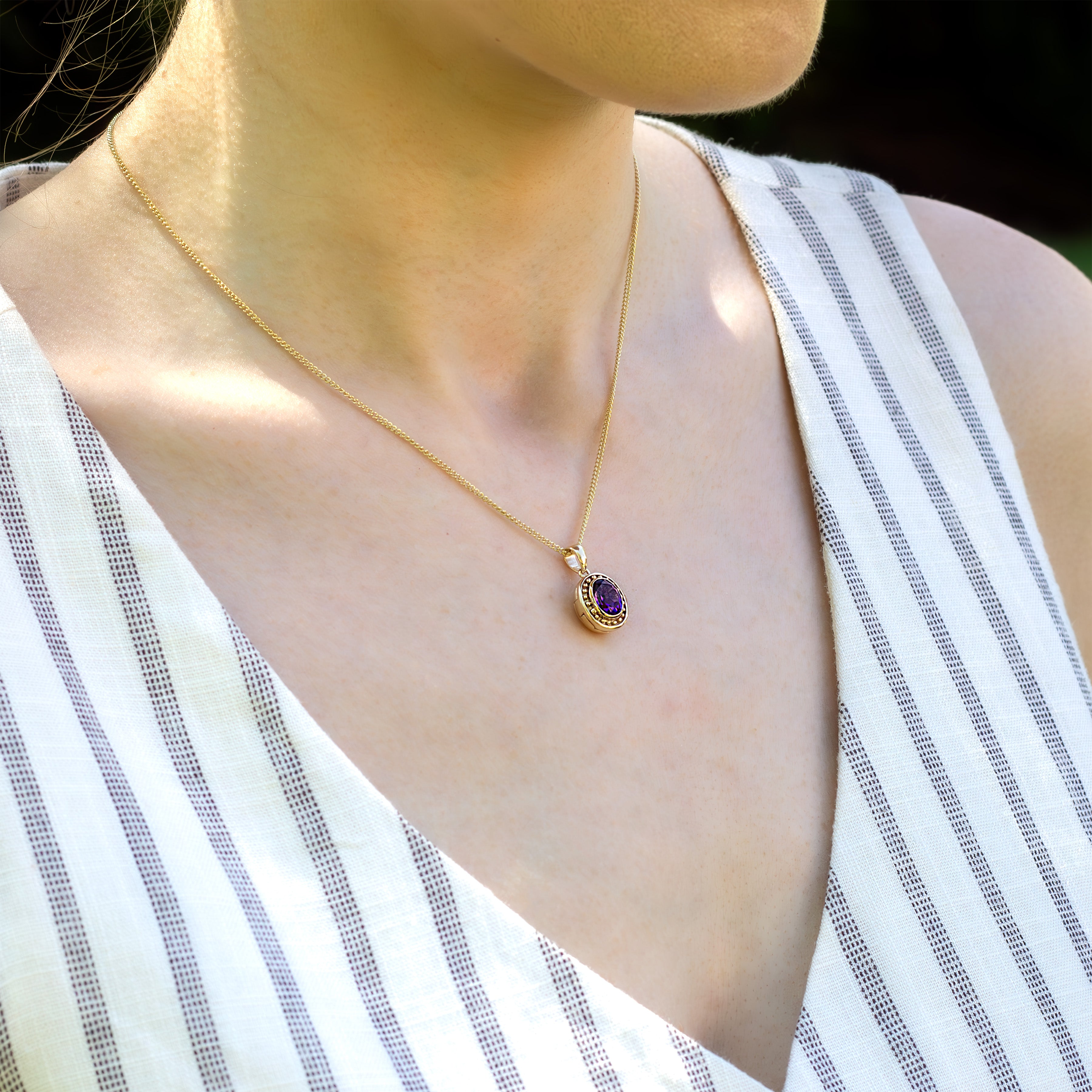 Photo of a model wearing a 9 ct gold locket with a vibrant purple amethyst in the middle and surrounded by gold beads on the edge of the locket placed on a 9ct rope chain.