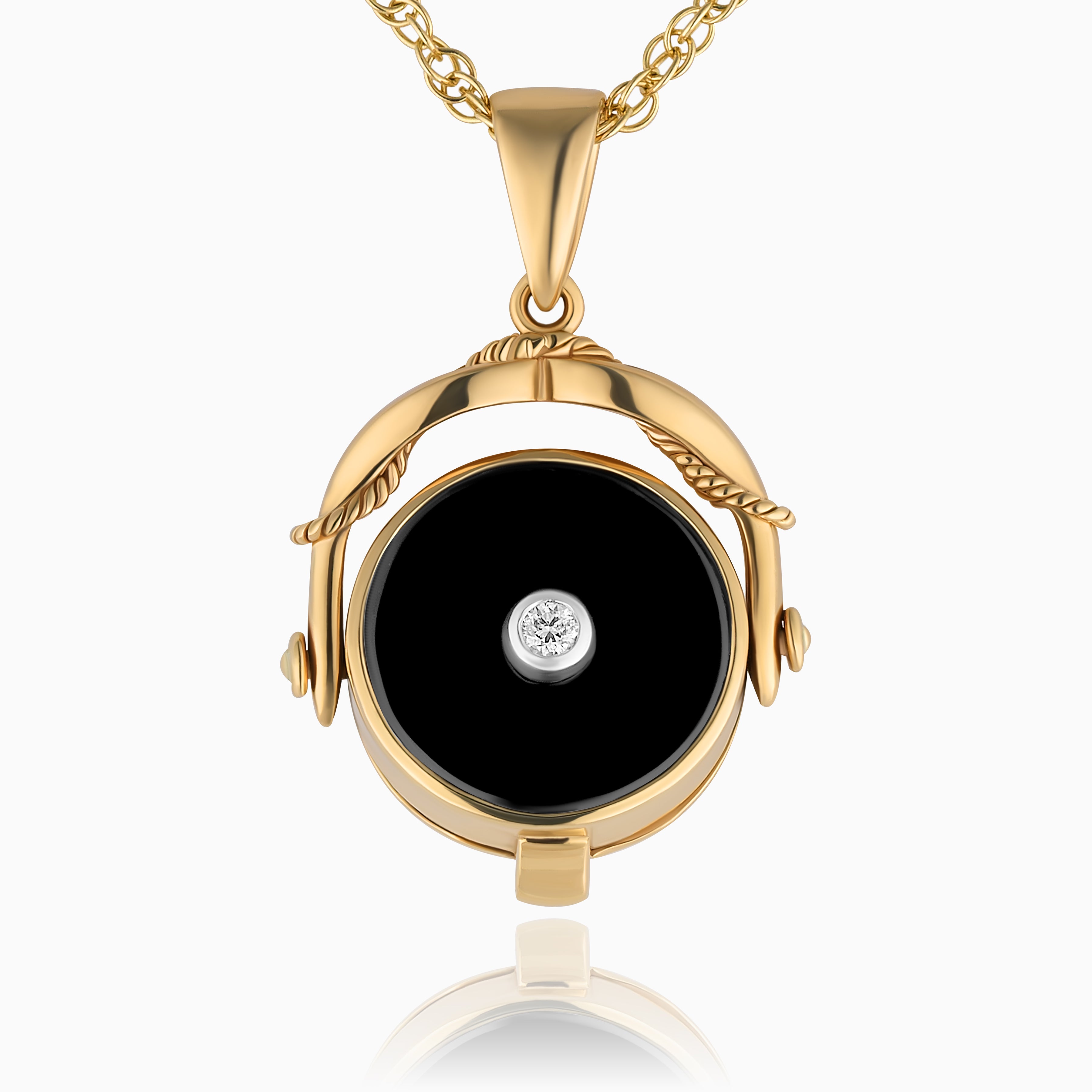 Close up photo of a gold vintage swivel locket with a black onyx base and a diamond in the middle and placed on a gold rope chain