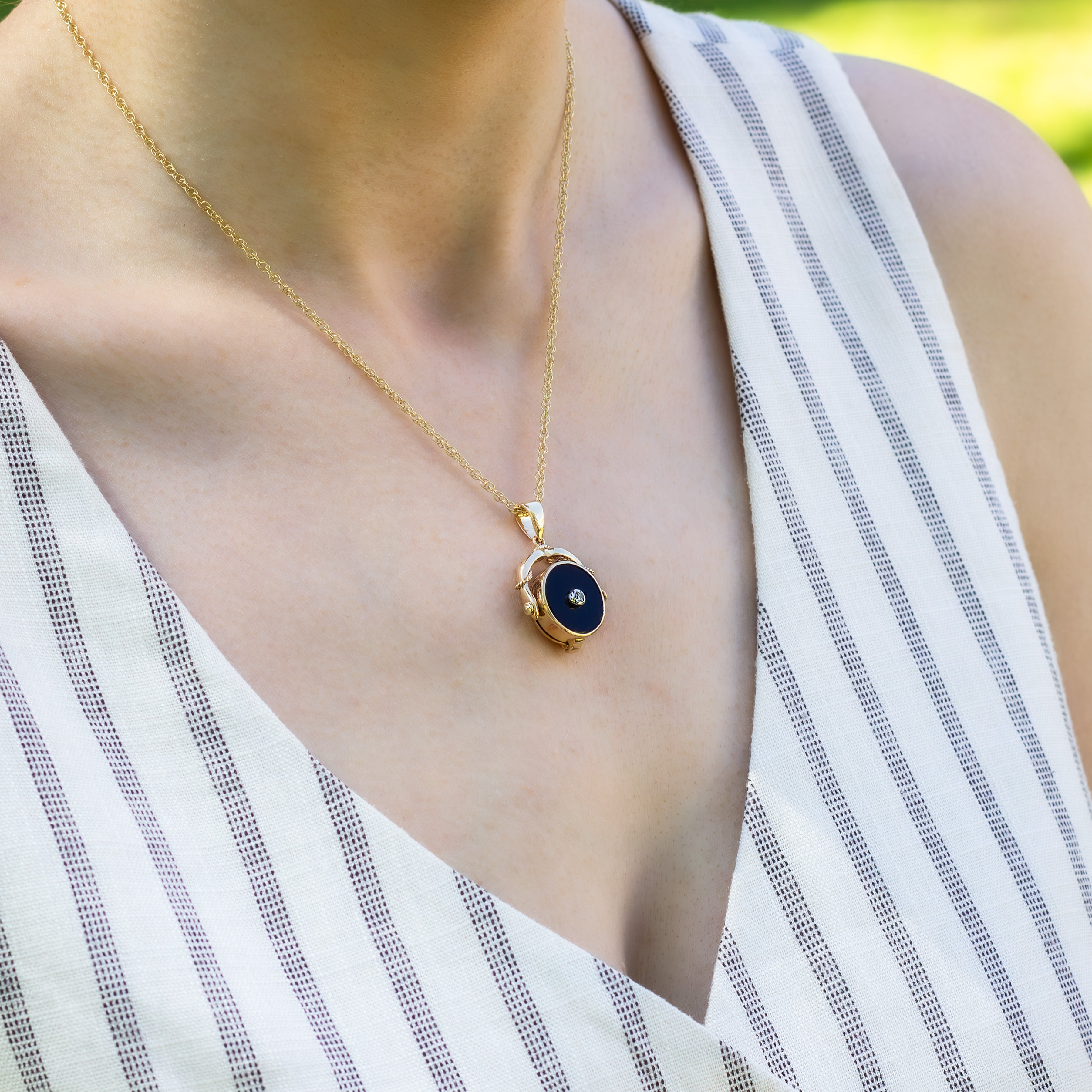 Model wearing a gold vintage swivel locket with a black onyx base and a diamond in the middle and placed on a gold rope chain