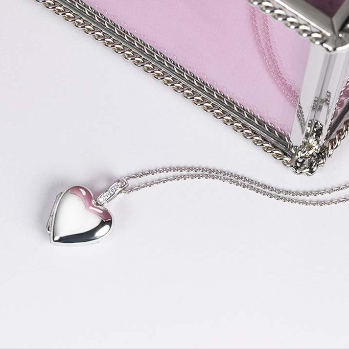 Platinum locket set with diamonds on the bail, alongside an jewellery box, on a white surface.