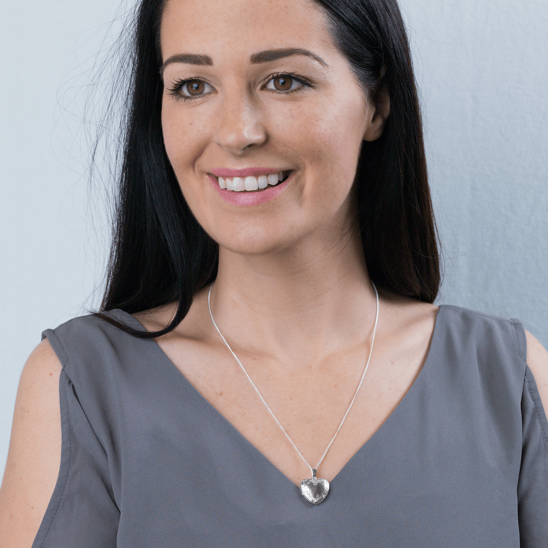 model wearing a 9 ct white gold heart shaped locket with a foliate border, on a 9 ct white gold curb chain