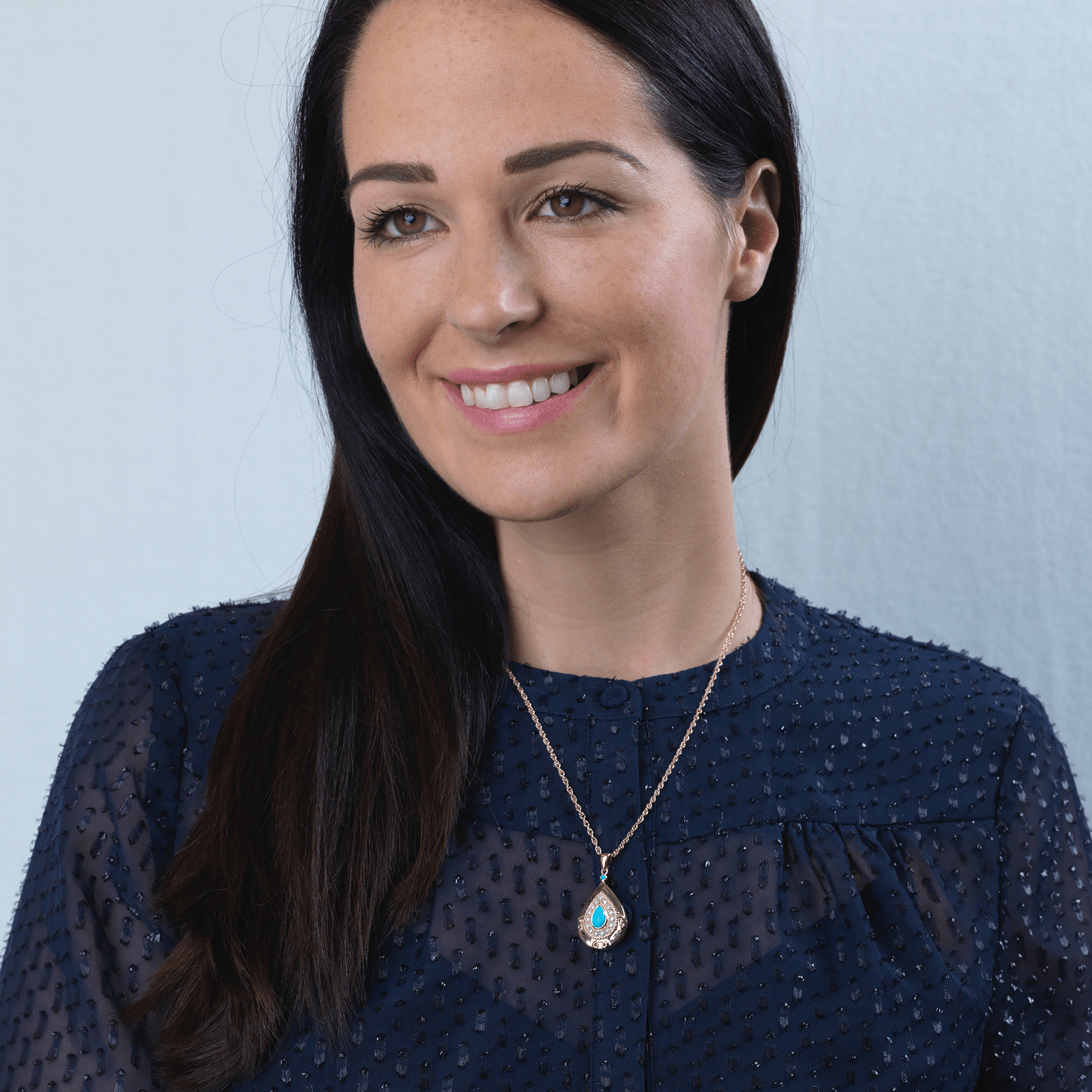 Model wearing a 9 ct gold teardrop shaped locket set with a turquoise cabochon surrounded by seed pearls, on a 9 ct gold rope chain