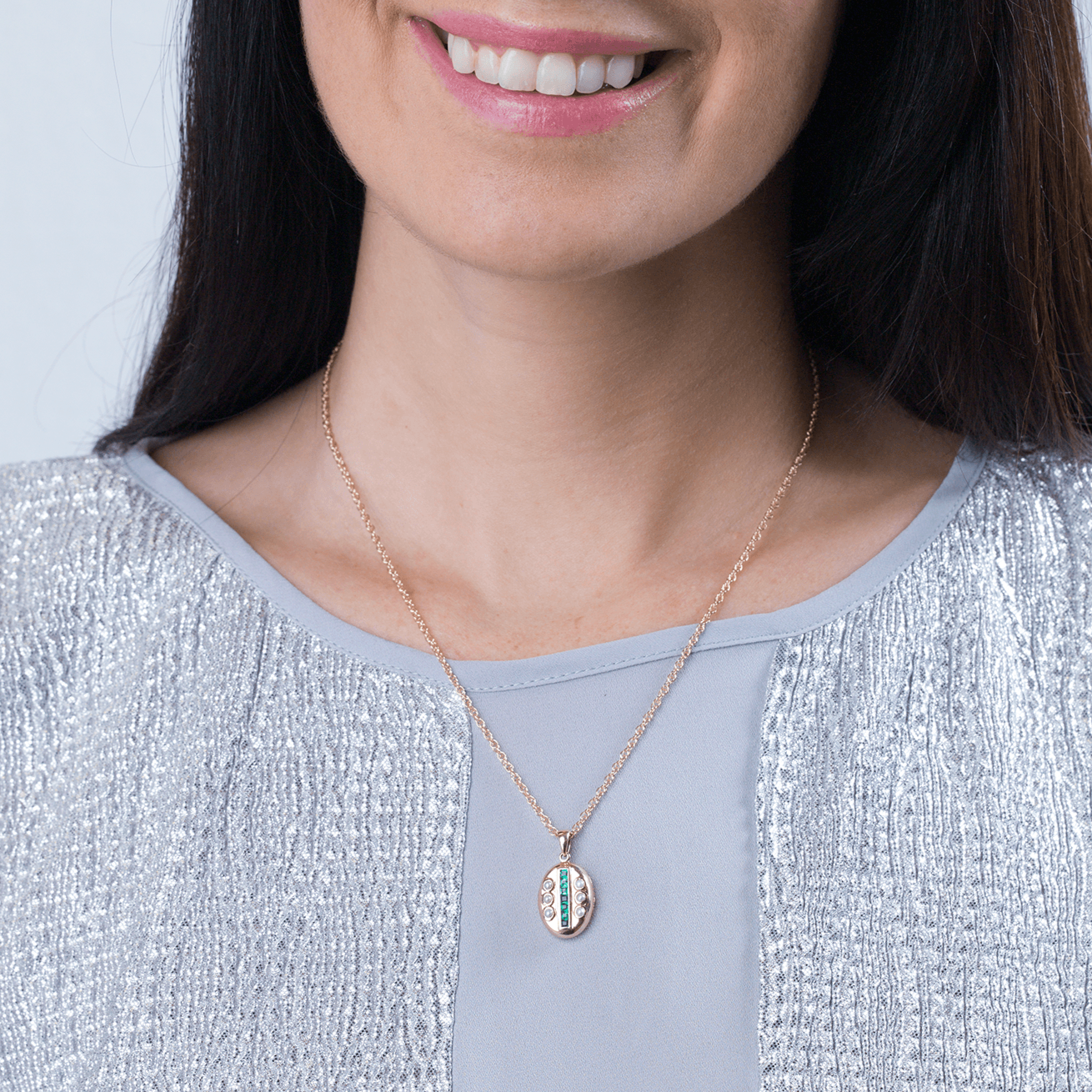 Model wearing a petite 9 ct gold oval locket set with emeralds and seed pearls on a 9 ct gold rope chain.