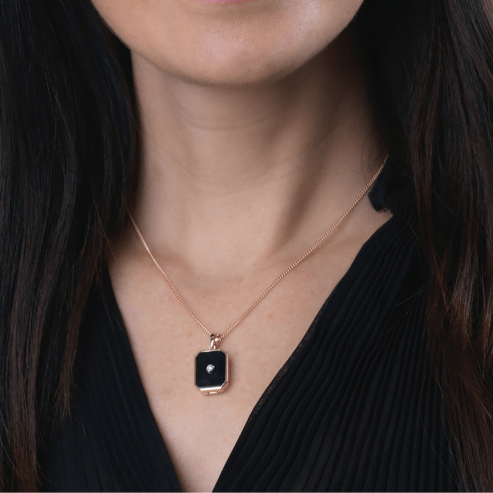 Model wearing a 9 ct rose gold tabular shaped locket set with a diamond on a black onyx plaque on a 9 ct rose gold rope chain