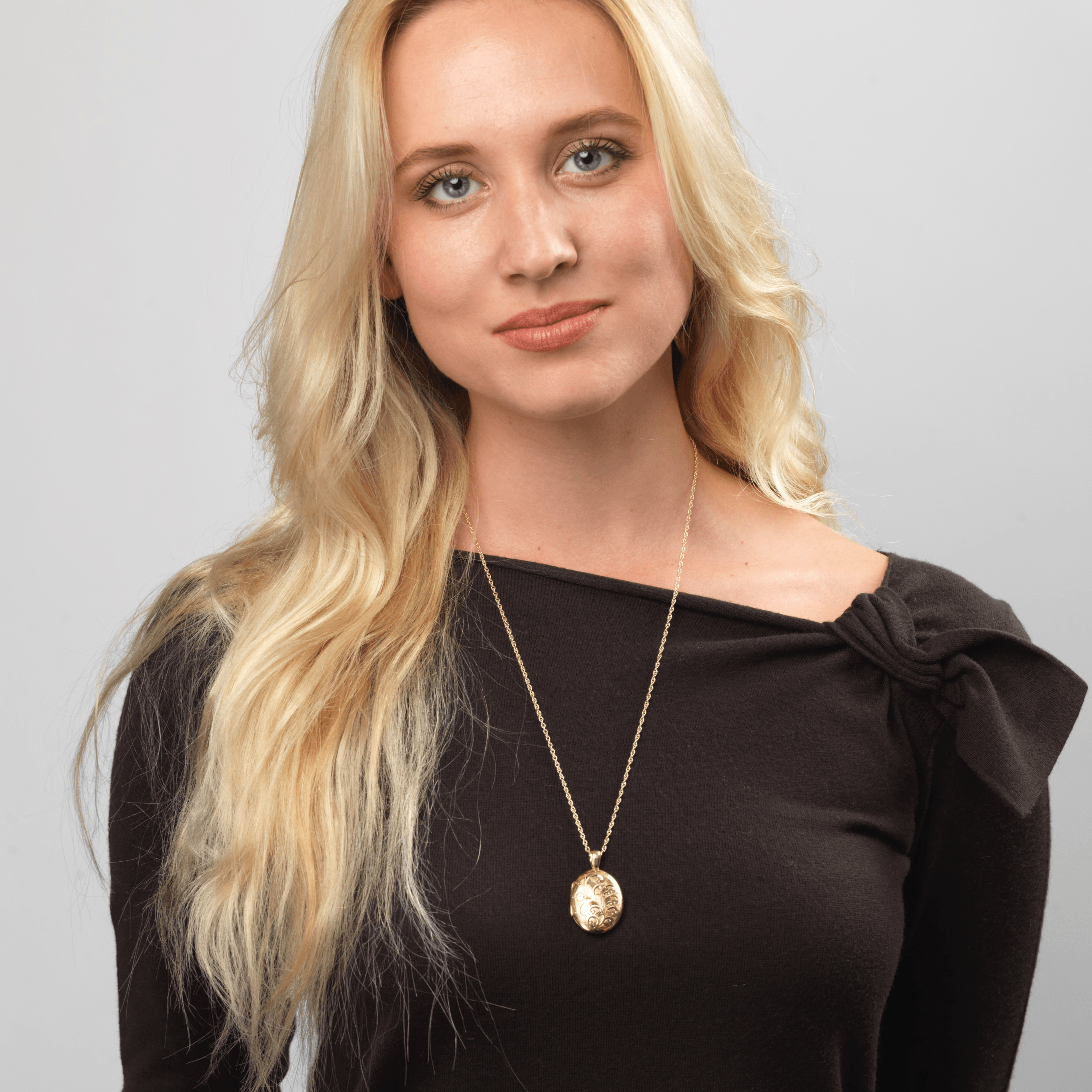 Model wearing an 18 ct gold oval locket engraved all over with a foliate design