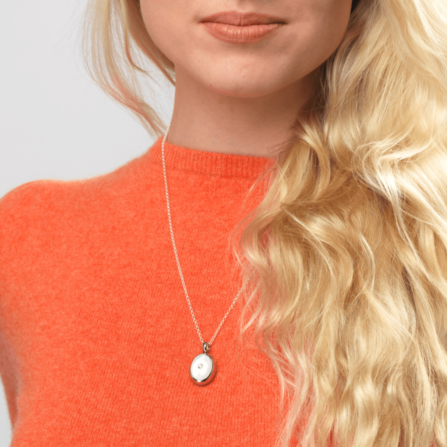 Model wearing an 18 ct white gold oval locket set with mother of pearl and a diamond in the centre, on an 18 ct white gold chain