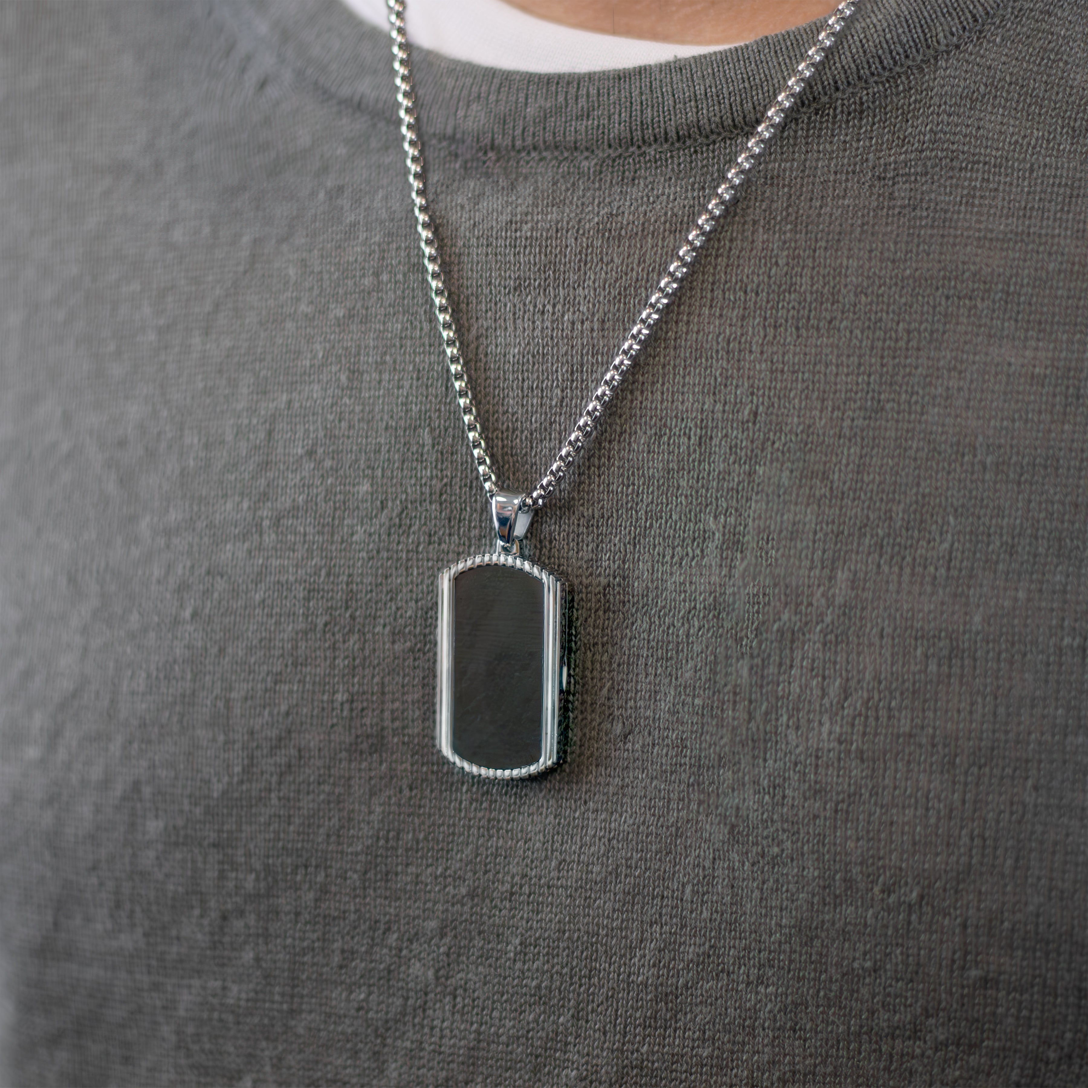 Model wearing a stainless steel and forged carbon fibre men's dog tag locket with a ridged edge and dark marble background placed on sterling silver chain