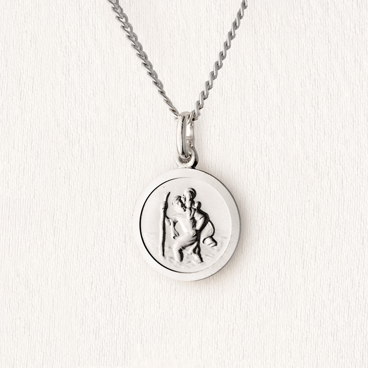A silver St. Christopher pendant necklace on a textured white background.
