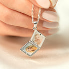Silver locket necklace with two photo frames held by a hand on a soft background