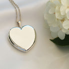 sterling silver heart locket on sterling silver rope chain lying on white silk next to a white flower 