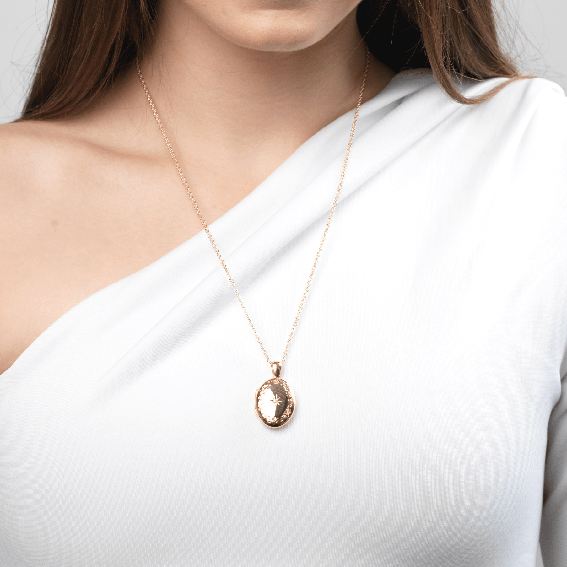 Model wearing an 18 ct gold oval locket engraved with a floral border and star set with a central diamond, on an 18 ct gold franco chain.