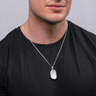 Model wearing a sterling silver dog tag shaped locket with a frosted finish, on a sterling silver curb chain