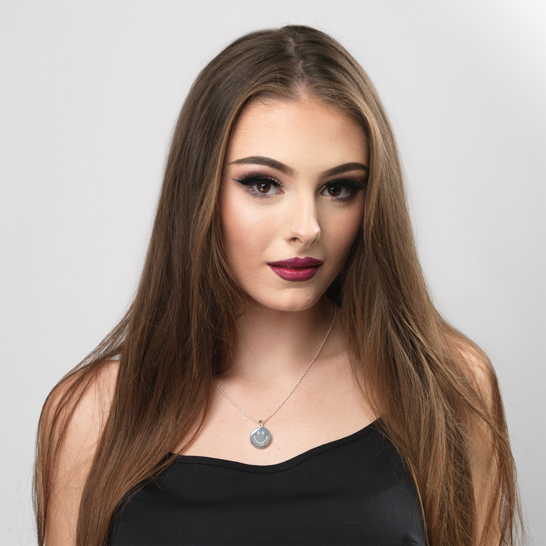 model wearing a sterling silver round locket with a smiley emoji engraved on the front