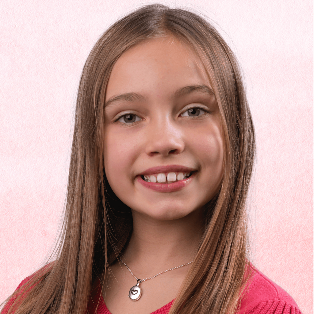 Child wearing a small oval sterling silver locket embossed with a heart on the front, on a sterling silver chain.