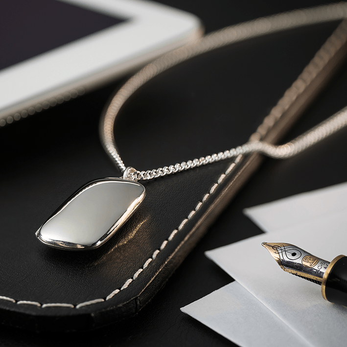 A 925 sterling silver dog tag shaped locket on a sterling silver curb chain, arranged on a black leather pad