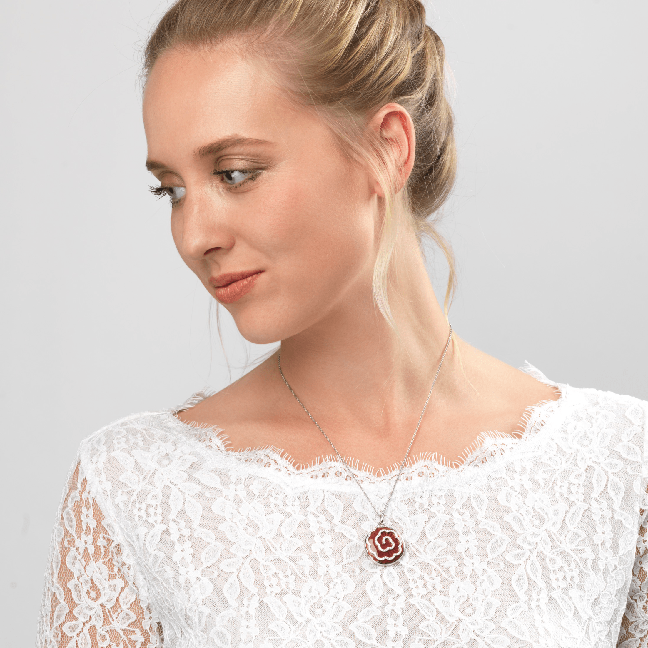Model wearing an 18 ct round locket with a red guilloche enamel background and daimonds aranged in a floral design, on an 18 ct white gold chain