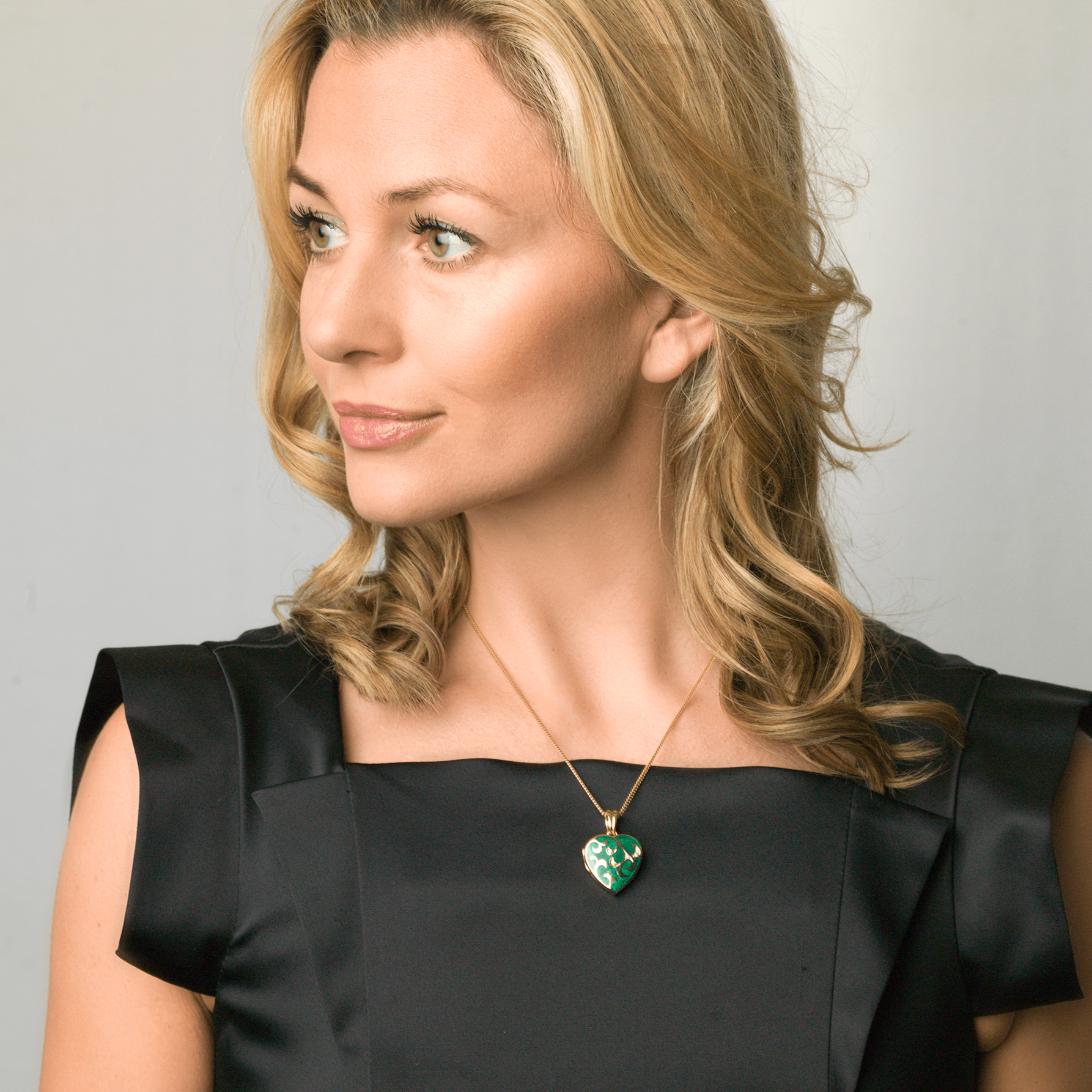 Model wearing an 18 ct gold heart locket set with green guilloche enamel and diamonds in a floral design on an 18 ct gold franco chain