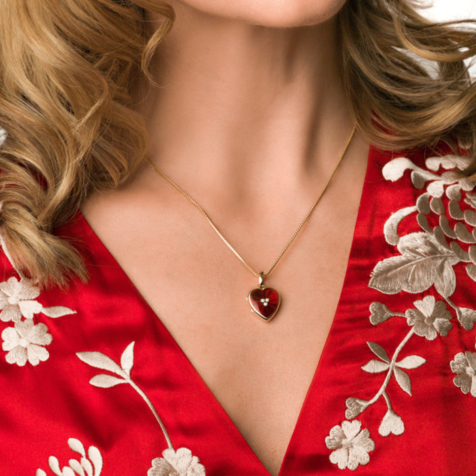 Model wearing an 18 ct gold heart locket set with red guilloche enamel and 3 central diamonds on an 18 gold chain