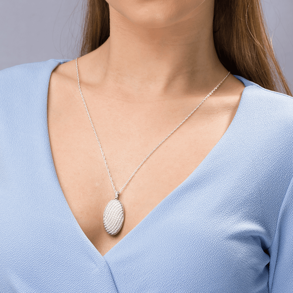 Model wearing an 18 ct white gold large oval locket pave set with diamonds in a swirling design, on an 18 ct white gold chain