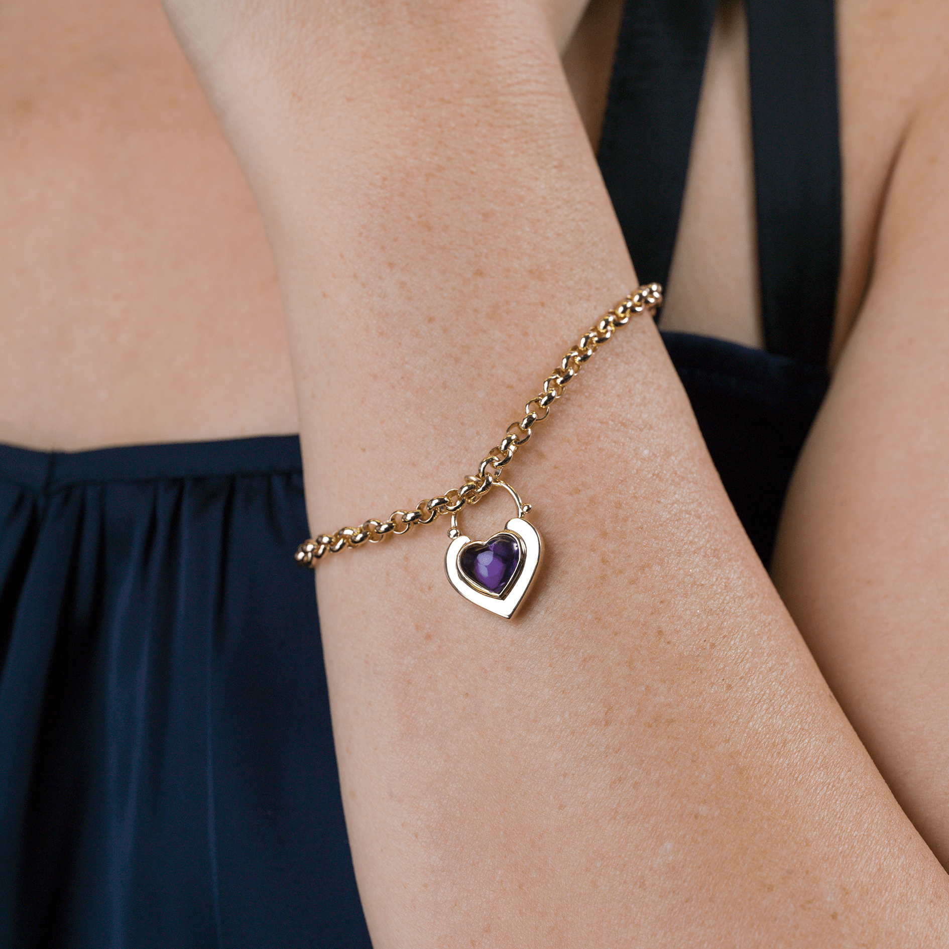 Model wearing a 9 ct gold padlock shaped locket set with a purple cabochon amethyst stone, on a 9 ct gold belcher bracelet