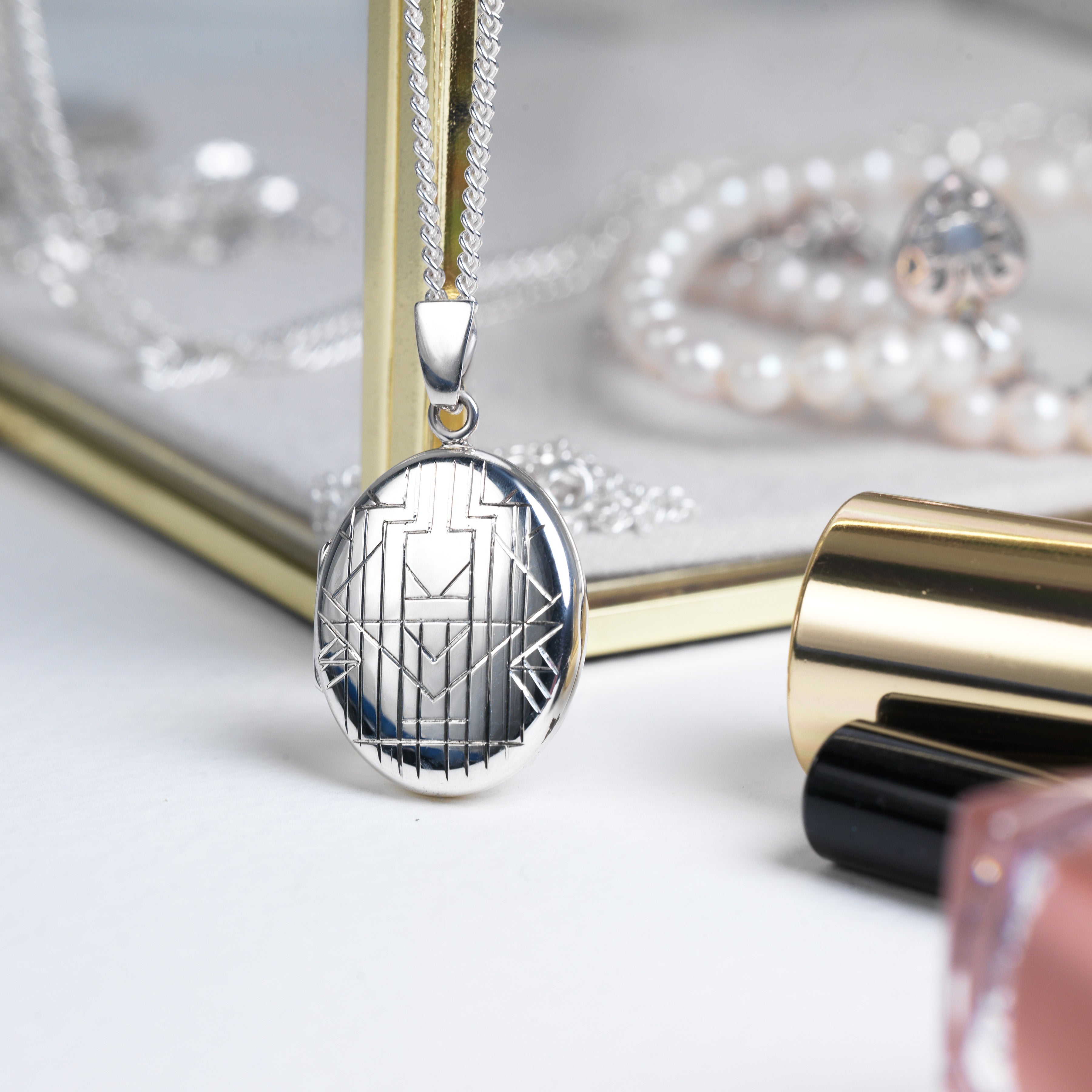 This is a stylized shot of a 925 sterling silver oval locket, hand engraved with an art deco chevron design on the front.