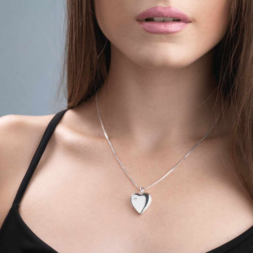 Model wearing a contemporary silver heart locket with a diamond on the left corner.