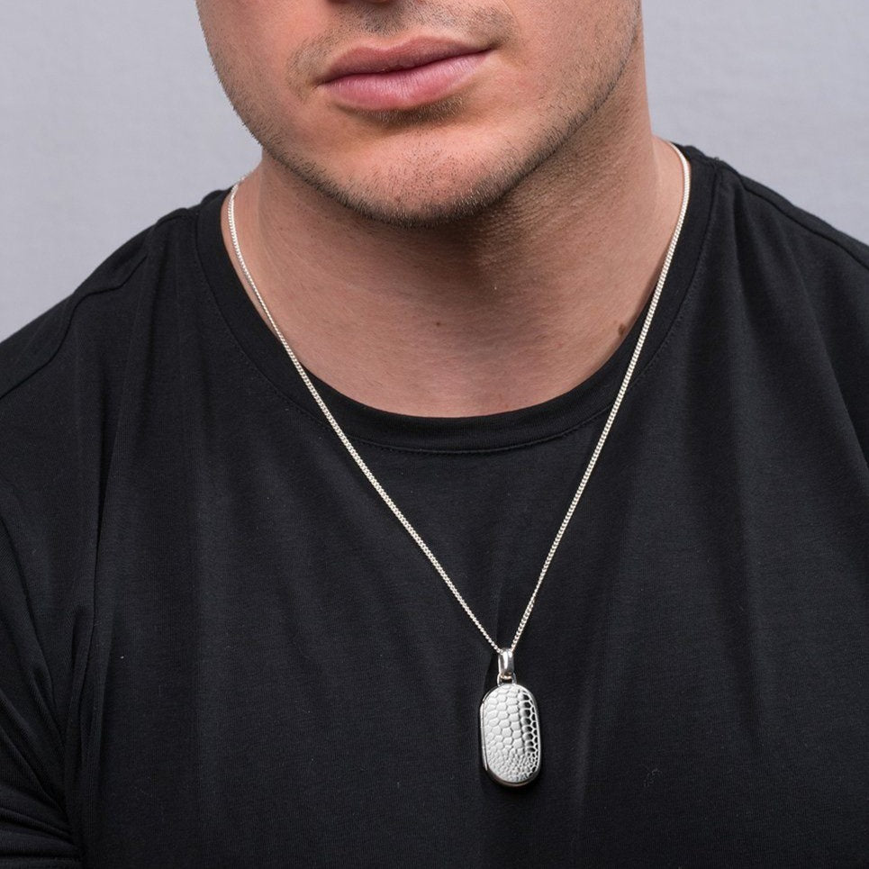 Model wearinga a sterling silver dog tag shaped locket embossed with a crocodile design on a sterling silver curb chain