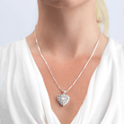 Model wearing a sterling silver heart locket set with pink mother of pearl surrounded by pierced out filigree