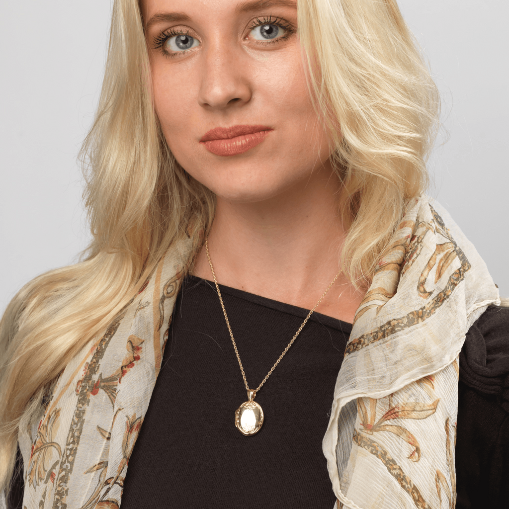 Model wearing an 18 ct gold oval locket engraved with a floral design at the top and bottom of the locket, on an 18 ct gold franco chain