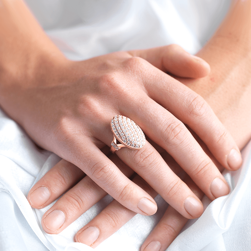 Model wearing an 18 ct rose gold oval locket ring pave set with diamonds in a swirling design. The shank is also set with diamonds.