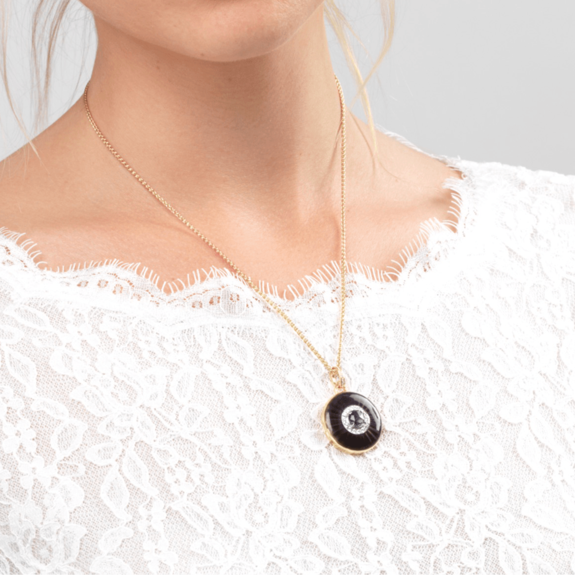 Model wearing an 18 ct gold round locket set with purple guilloche enamel, a purple amethyst stone and diamonds. The bail is also set with diamonds. On an 18 ct gold chain.