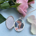 open shot of a large oval sterling silver locket showing a wedding photo, on a background showing a pink rose