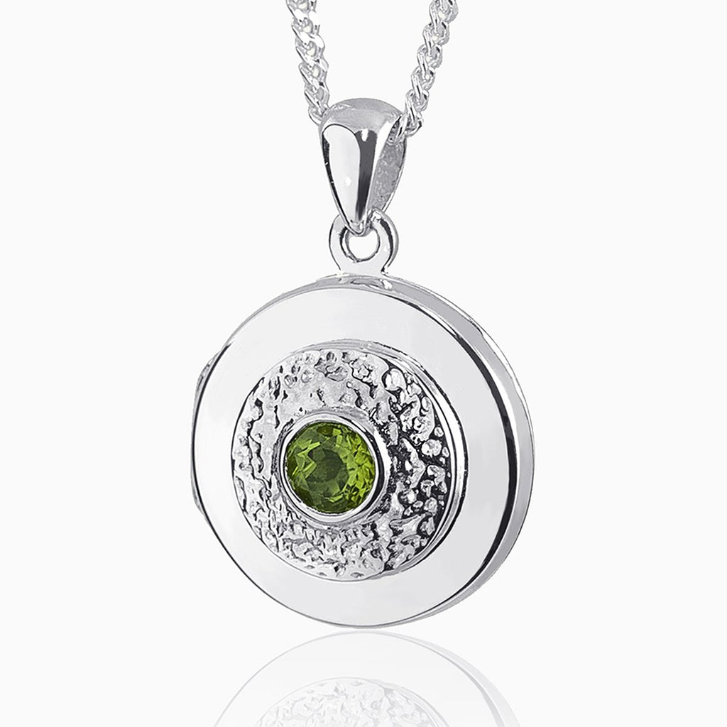 round 9 ct white gold locket set with a central peridot and surrounded by an engrved pattern on a 9 ct white gold curb chain