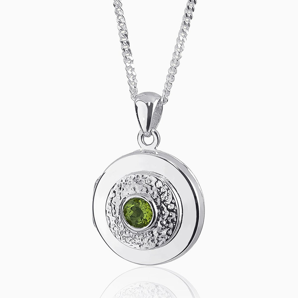 round 9 ct white gold locket set with a central peridot and surrounded by an engrved pattern on a 9 ct white gold curb chain